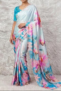 A woman models a light blue saree with a vibrant pink, blue, and white floral print, paired with a matching light blue blouse, set against a white faux fur backdrop.