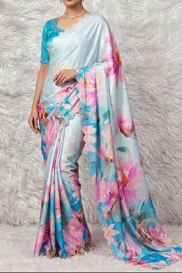 A woman models a light blue saree with a vibrant pink, blue, and white floral print, paired with a matching light blue blouse, set against a white faux fur backdrop.