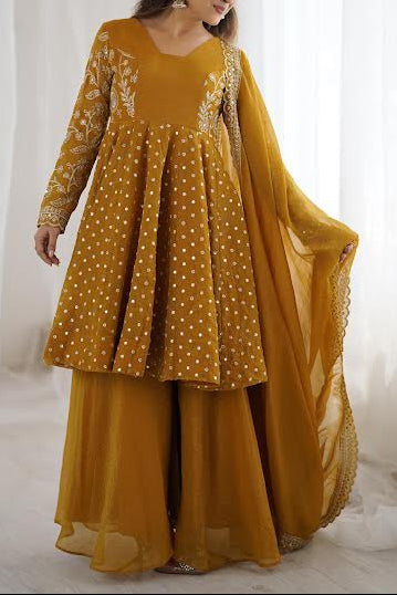 Woman wearing a mustard yellow traditional outfit with white patterns against a white curtain background
