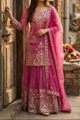 Woman in a pink embroidered traditional outfit standing in an alleyway.